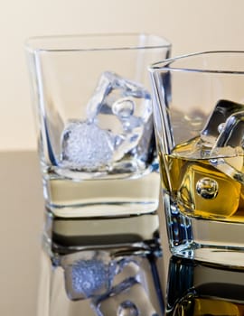 one glass of whiskey and one empty with ice cubes on table with reflection, time of relax with whisky