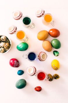 Easter eggs and jars with colored liquid from above on white background