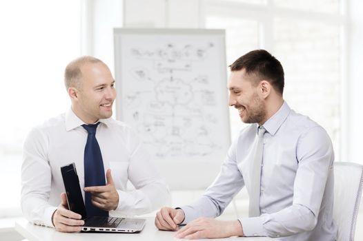 business, technology and office concept - two smiling businessmen with laptop having presentation in office