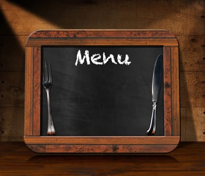 Old blackboard with wooden rectangular frame, silver cutlery and text Menu on a wooden table and wooden wall. Template for recipes or food menu