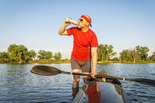 senior kayak paddler drinking water or sport drink after paddling workout on a lake in summer