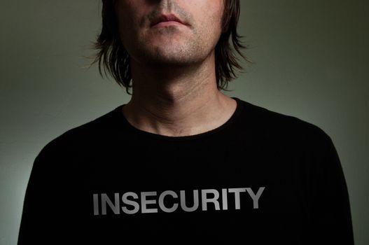Man wearing a black shirt with "Insecurity" title on his chest. Shiness, insecurity, solitude concept image.