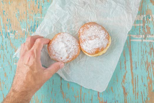 Hand reaches for sweet sugary donut on rustic table