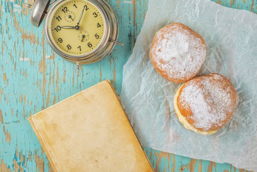 Sweet sugary donuts, book and vintage clock on rustic table
