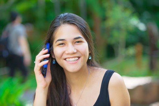 Biracial teen girl talking on cell phone outdoors