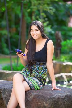 Biracial teen girl sitting on rock looking at cellphone