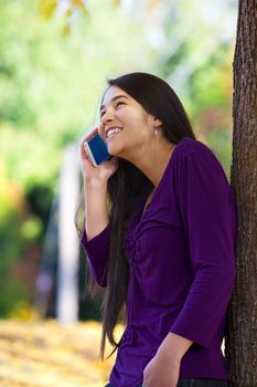 Teen girl standing against autumn tree talking on cell phone