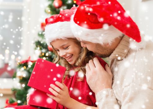 christmas, holidays, family and people concept - smiling father and daughter in santa hats opening gift box at home