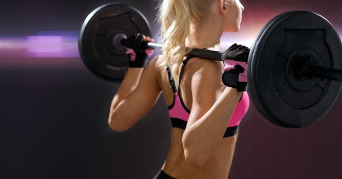 sporty woman exercising with barbell from back