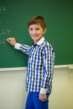 little smiling schoolboy writing on chalk board