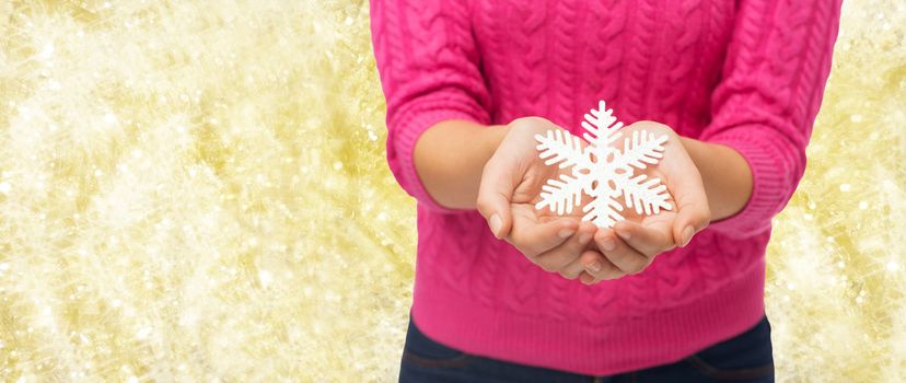 christmas, holidays and people concept - close up of woman in pink sweater holding snowflake decoration over yellow lights background