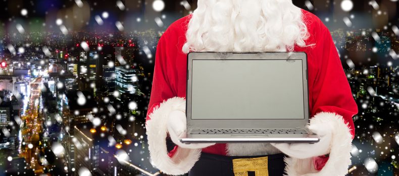 christmas, advertisement, technology, and people concept - close up of santa claus with laptop computer over snowy night city background