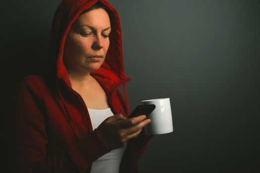 Beautiful red hooded woman drinking coffee and sending text mess