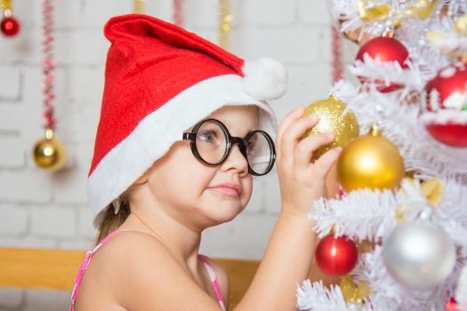 Girl with round glasses hangs balls on a snowy New Years Christmas tree