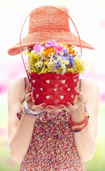 Woman with basket of wildflowers in hands. Young blonde boho girl in orange hat on summer meadow, people. Attractive joyfull, romantic style, floral sundress. Sunny day