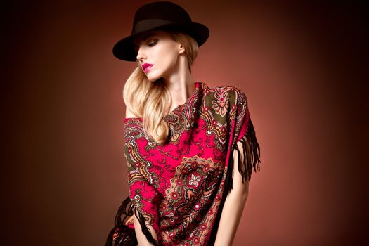 Fashion beauty woman in stylish hat, colored cashmere shawl. Autumn winter model blond girl with long blonde wavy hair, ethnic pattern headscarf. Unusual creative attractive people. Retro Vintage