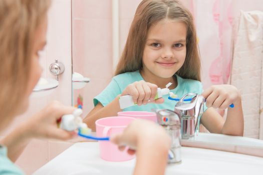 Six year old girl squeezes the toothpaste from a tube on toothbrush