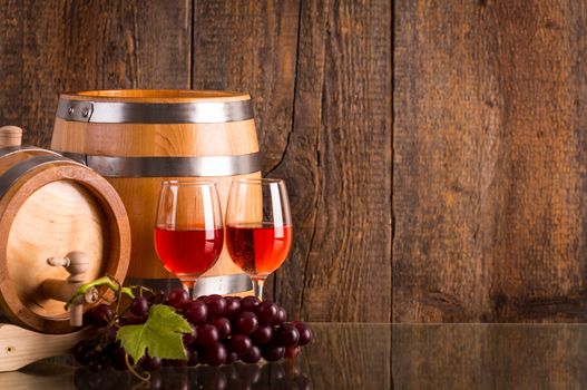 Two glasses of rosé wine with two barrels and grapes