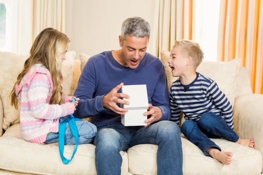 Father opening gift given by children on sofa
