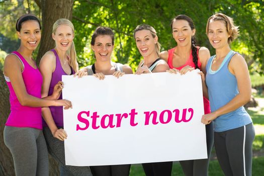Start now against fitness group holding poster in park