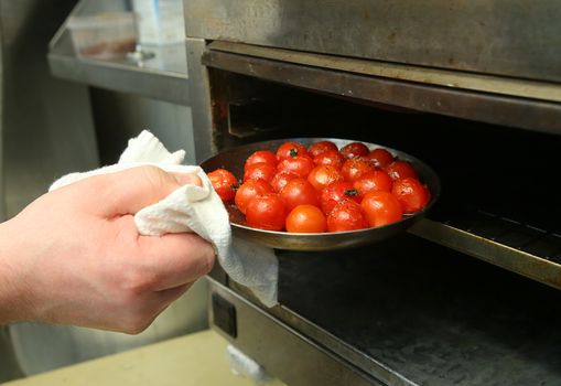 The man pulls out of the oven baked tomatoes