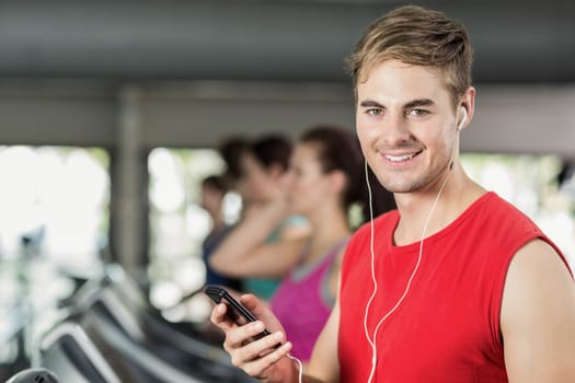 Smiling muscular man on treadmill listening to music