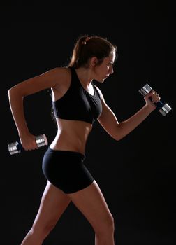 Young woman doing exercise with dumbbells, over black