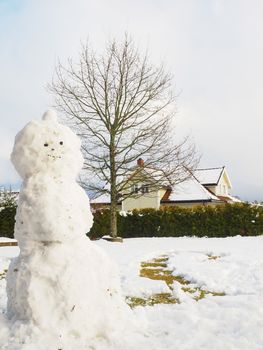Snowman in garden half done, without scarf, hat and carrot in fr