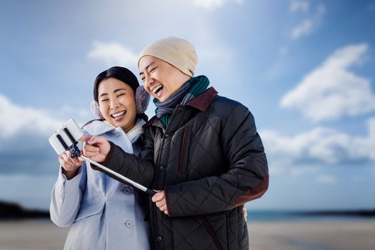 Couple laughing at their pictures taken on smartphone against beach with blue sky