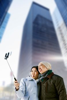 Composite image of playful couple taking selfie against building