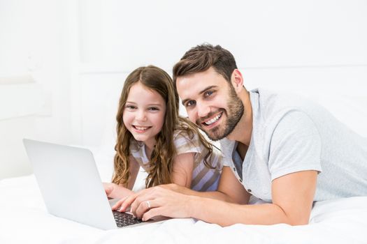 Happy father and daughter using laptop on bed