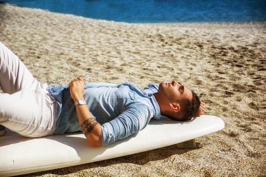Handsome man lying on surfboard at beach