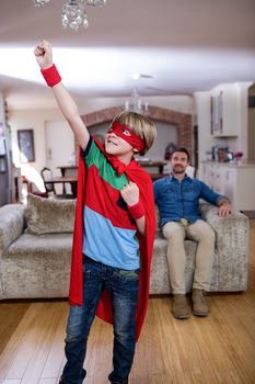 Son pretending to be a superhero while father sitting on sofa