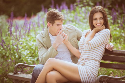 Loving young couple flirting while sitting at a park bench.
