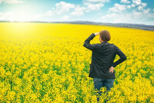 Woman agronomist standing in field of blooming cultivated rapese