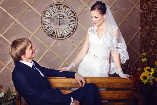Bride and groom sitting on a bench in studio with vintage interior. Photo of happy newlyweds