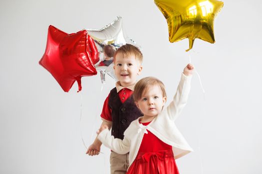 Little kids holding balloons in the form of stars. Children holding a star-shaped balloons. Happy children with colorful shiny foil balloons against a white background