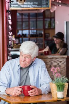 Grumpy mature man sitting by himself in a coffee house