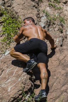 Handsome, muscular, shirless climber climbing rock