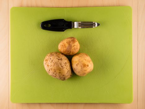 Three potatoes and peeler on green plastic board