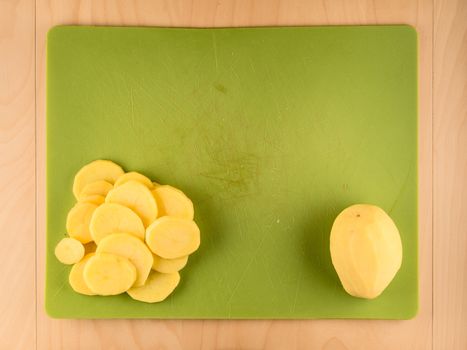 Whole and sliced potatoe on green plastic board