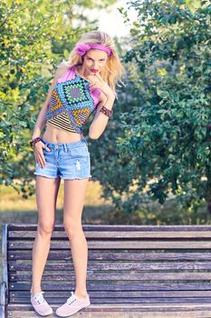 Beauty stylish playful woman on bench, park, people, outdoors.Attractive hipster happy pretty blonde girl with bow, fashionable top, denim shorts. Relax in summer garden,lifestyle