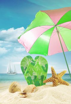 Sandals and seashells with umbrella at the ocean