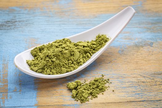 white spoon of organic matcha green tea powder against grunge wood