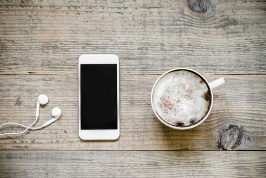 Cup of cafe latte with smartphone and earphones on wooden table