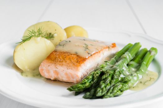 Grilled salmon with boiled potatoes and asparagus on white plate