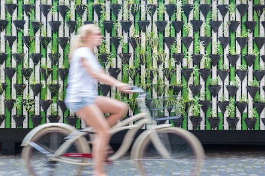 Woman riding bycicle by green urban vertical garden wall.