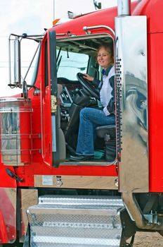 Woman truck driver looking out the door of a big rig from the driver's seat