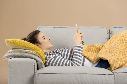 Beautiful woman at home lying on the sofa and using a phone