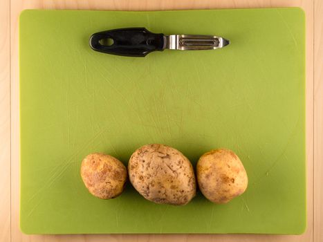 Three unpeeled potatoes on green plastic board